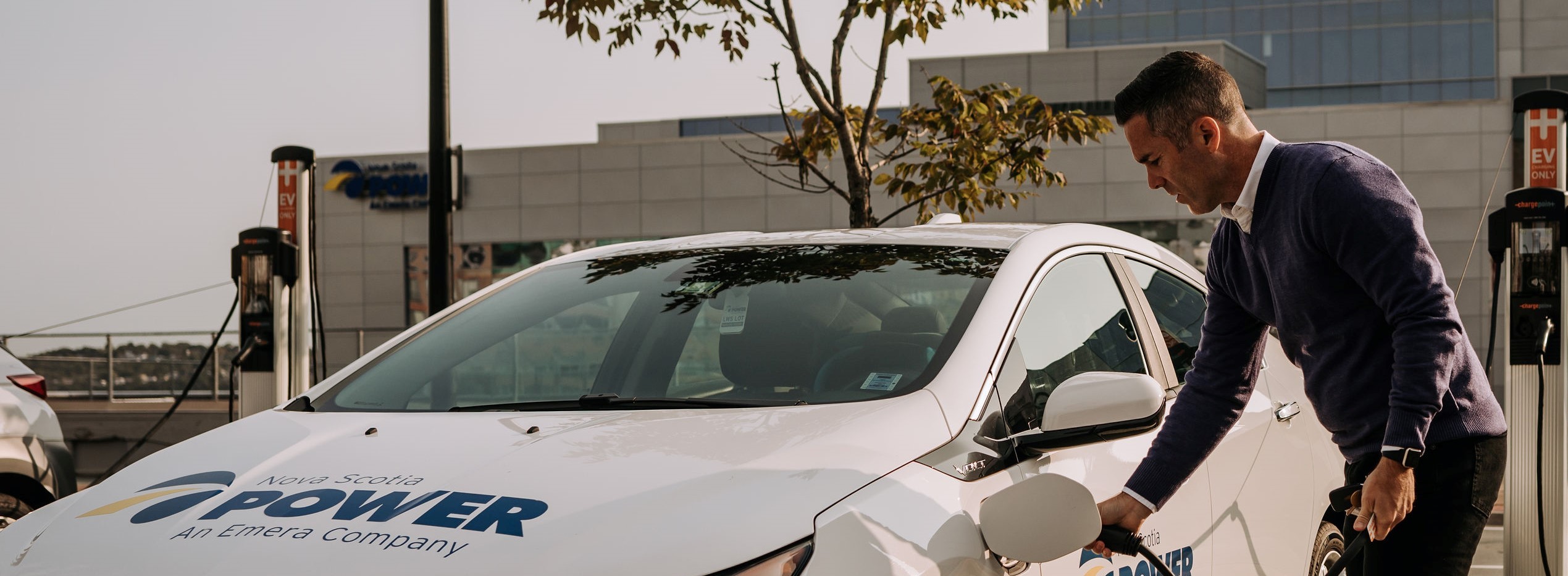 A man charging a car which has the Nova Scotia Power brand logo on its hood