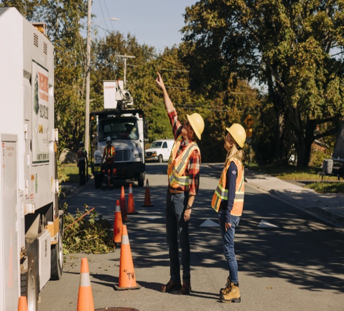 Workers taking safety precautions while performing their tasks. They are wearing protective helmets and jackets to ensure safety.