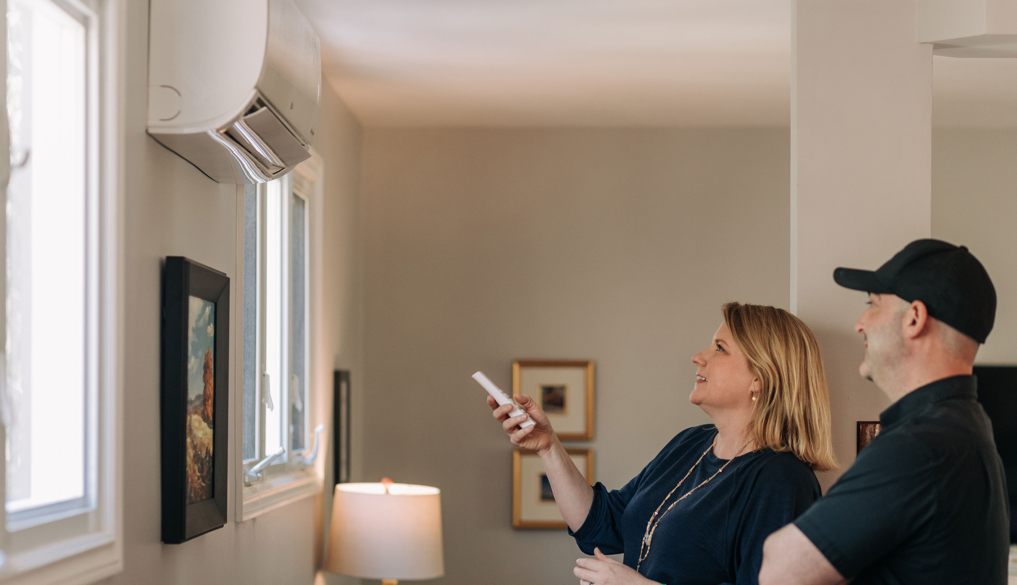 customer-pointing-remote-at-heat-pump-with-contractor