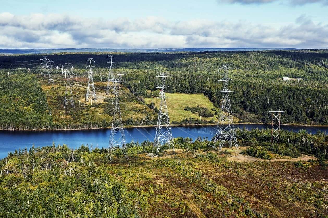 Power transmission lines over a beautiful green landscape with a river flowing in between